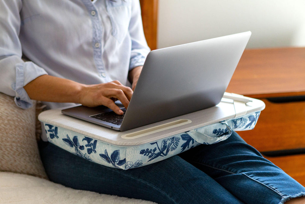 Person working on a laptop with the Blue Blossom Designer Lap Desk on their lap, providing comfort and stability while resting on a bed.