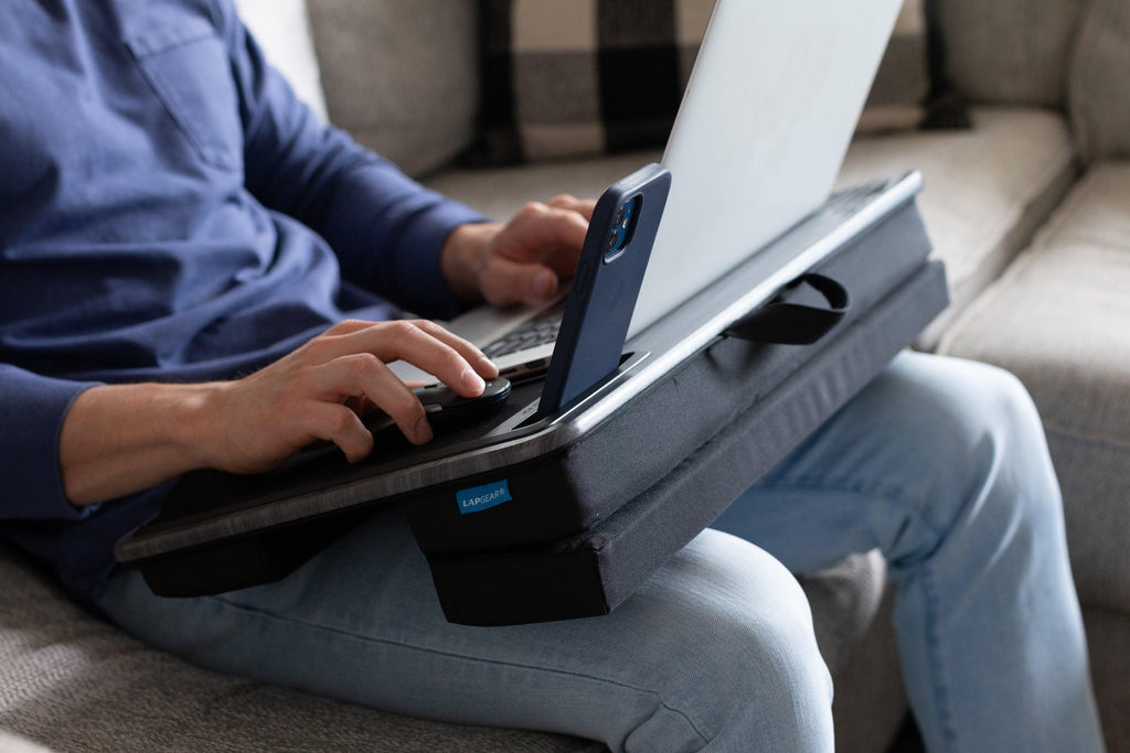 Person sitting on a couch using the Elevation Pro Lap Desk on their lap, working on a laptop with an adjustable height feature for ergonomic comfort.