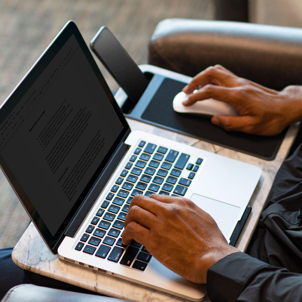 Person sitting in a chair using the White Marble Home Office Lap Desk on their lap, working on a laptop with the built-in mouse pad, and phone holder.