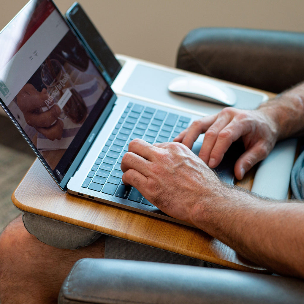 Person sitting in a chair using the Oakwood Home Office Pro Lap Desk on their lap, working on a laptop with the built-in mouse pad, phone holder, and cushioned wrist rest for added comfort.