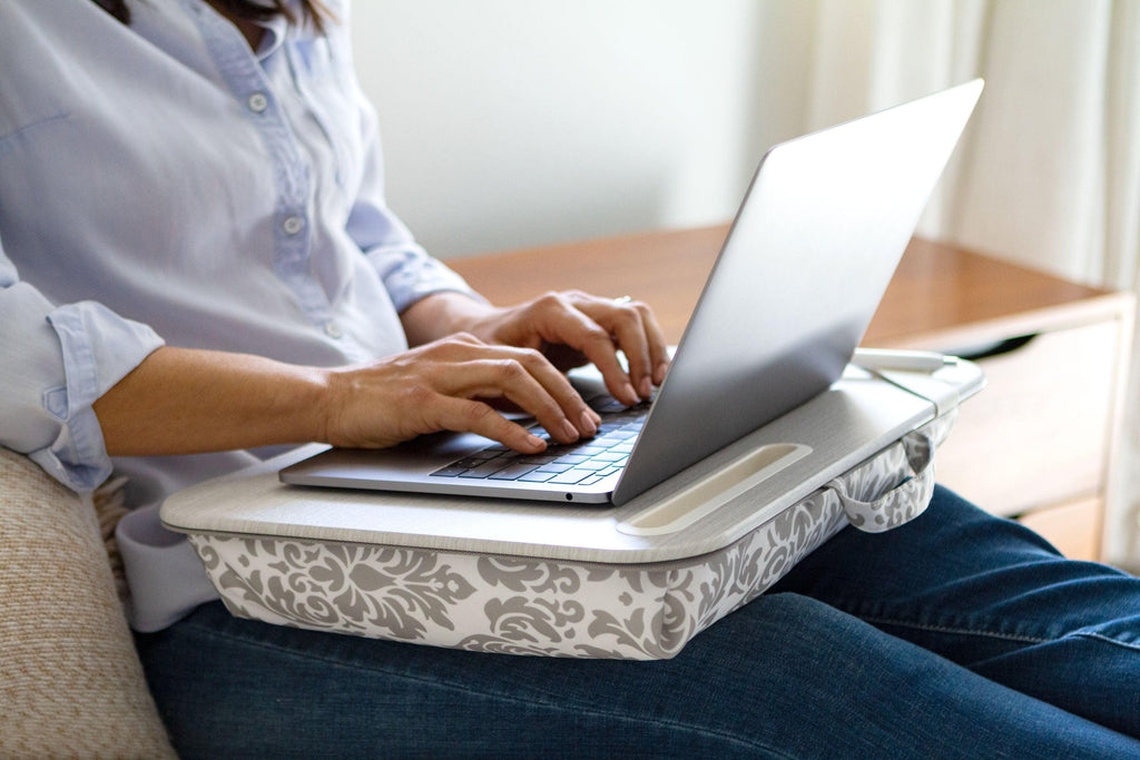 Person working on a laptop with the Gray Damask Designer Lap Desk on their lap, providing comfort and stability while resting on a bed.